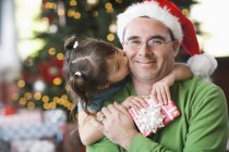 Tochter umarmt und küsst Vater im Weihnachtsmann-Hut — Stockfoto