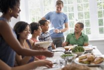 Сім'я чоловіків, жінок і хлопчиків обмінюються їжею за обіднім столом . — стокове фото
