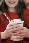 Close-up de xícara cheia de marshmallows frescos em mãos de menina pré-adolescente . — Fotografia de Stock