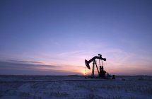 Appareil de forage pétrolier et cric de pompage dans une plaine plate du champ pétrolifère canadien au coucher du soleil
. — Photo de stock