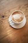 Cup of frothy cappuccino in cup with saucer on wooden table. — Stock Photo