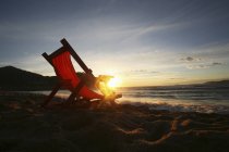Lounge chair on sand facing sea water at sunset . — Stock Photo