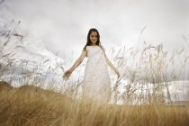 Elementary age girl in white dress standing in grass with arms outstretched — Stock Photo