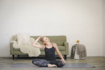 Donna bionda in body nero e leggings seduta su tappetino yoga in camera — Foto stock