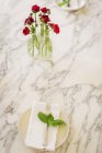Mármore mesa e vaso de flores vermelhas cortadas frescas e guardanapo com manjericão . — Fotografia de Stock