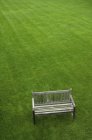 High angle view of wooden bench on green grass lawn. — Stock Photo