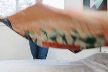 Mulher jogando colcha sobre cama de casal no quarto . — Fotografia de Stock