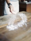 Female hand spreading flour across wooden tabletop. — Stock Photo