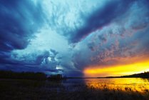 Pôr do sol no horizonte sobre o lago com nuvens de tempestade nascentes . — Fotografia de Stock