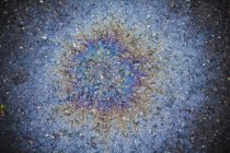 Spilled oil radiating pattern with multicolored effect on road. — Stock Photo