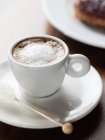 Xícara de cappuccino espumoso na xícara com pires na mesa de madeira . — Fotografia de Stock