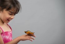 Chica asiática sosteniendo mariposa en la mano sobre fondo gris . - foto de stock