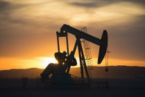 Pumpjack working at oil drilling site at sunset. — Stock Photo