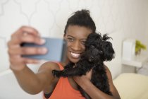 Девочка-подросток делает селфи с маленькой черной собакой на смартфоне . — стоковое фото