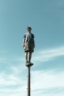 Uomo in equilibrio su palo metallico contro cielo blu con nuvole . — Foto stock