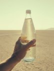 Mão masculina segurando garrafa de água na paisagem do deserto de Black Rock em Nevada — Fotografia de Stock
