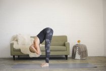 Donna bionda in piedi su tappetino yoga e piegandosi in avanti con le braccia dietro la testa . — Foto stock