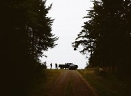 Route de campagne avec véhicule stationné au sommet et silhouette de deux personnes . — Photo de stock