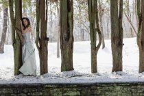 Giovane donna in abito da ballo all'aperto nella neve tra gli alberi . — Foto stock