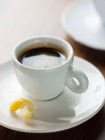 Close-up of cup of black coffee in white cup with twist of lemon peel in saucer. — Stock Photo