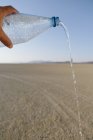 Männliche Hand gießt Wasser aus Flasche in Landschaft schwarzer Felswüste in Nevada — Stockfoto