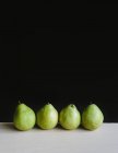 Row of four green Anjou pears on table — Stock Photo