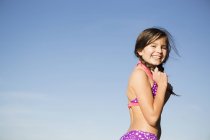 Pre-adolescent girl in pink swimwear with plaited hair against blue sky. — Stock Photo