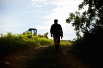 Silhueta de agricultor masculino caminhando para o campo com trator . — Fotografia de Stock