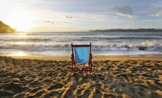 Пляжний стілець на піску і заході сонця на горизонті над морем . — стокове фото