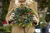 Cropped view of woman carrying decorated wreath of holly and evergreen leaves. — Stock Photo