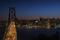 Ponte di notte con traffico illuminato e luci di insediamenti lungo la riva della baia a San Francisco, USA
. — Foto stock