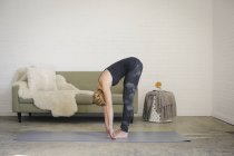 Mulher loira dobrando-se para a frente no tapete de ioga em casa interior . — Fotografia de Stock