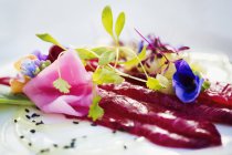Carpaccio y guarnición de brotes de guisantes frescos y flores comestibles en plato blanco . - foto de stock