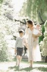 Mulher adulta média com filho e filha andando no jardim . — Fotografia de Stock