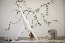 Mujer rubia sobre estera de yoga blanca inclinándose con la pierna levantada . - foto de stock