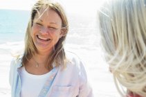Smiling blonde mature woman standing by ocean with friend. — Stock Photo