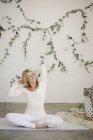 Donna sorridente seduta su tappetino yoga bianco e braccia tese . — Foto stock