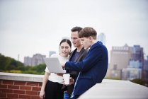 Young woman and men standing on rooftop and using laptop computer together. — Stock Photo