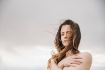 Woman with long brown hair standing against cloudy sky. — Stock Photo