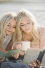 Two teenage sisters lying on jetty, reading books and holding cup. — Stock Photo