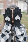Jovem mulher escondendo o rosto atrás das mãos em luvas de lã com design em forma de coração . — Fotografia de Stock