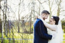 Braut und Bräutigam lachen und umarmen sich im Garten, Seitenansicht. — Stockfoto