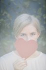Portrait of woman holding red heart shape in front of face. — Stock Photo