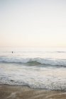 Океанічна хвиля котиться на піщаному пляжі з людиною на фоні . — стокове фото