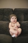 Ребенок сидит на диване в подгузнике и вязаной шляпе . — стоковое фото