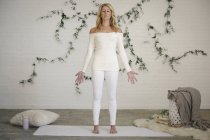Blonde woman in a white leotard and leggings standing on white mat in room. — Stock Photo