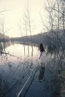 Frau in weißem Kleid steht in der Abenddämmerung am Ufer des Sees im flachen Wasser. — Stockfoto