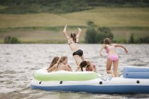 Teenage girls jumping and having fun on inflatable dinghy on lake. — Stock Photo