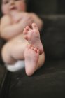 Close-up of feet of baby lying on sofa in diaper. — Stock Photo