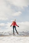 Teen girl in red jacket leaping in air above snow outdoors. — Stock Photo